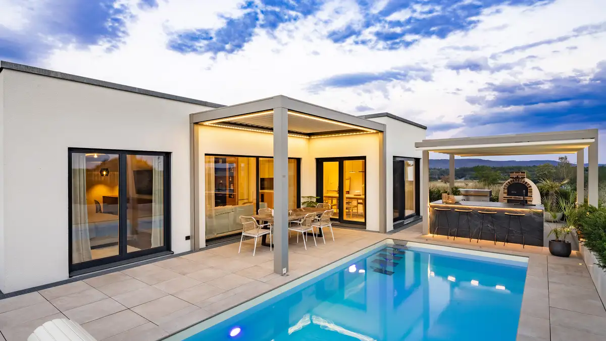 Flachdachbungalow von der Gartenseite mit Pool, Blick auf die überdachte Terrasse, Bungalow in leichter L-Form, Aufnahme bei Dämmerung