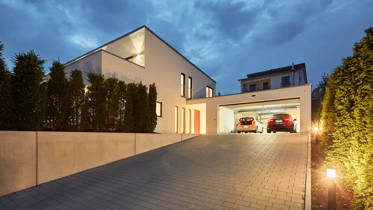 Pultdachhaus in leichter Hanglage, hier wurde das Haus auf ebenem Grund gebaut, die Einfahrt führt dem Hang hinauf, Hofeinfahrt mit Garage, linkerhand das Pultdachhaus mit roter Haustüre