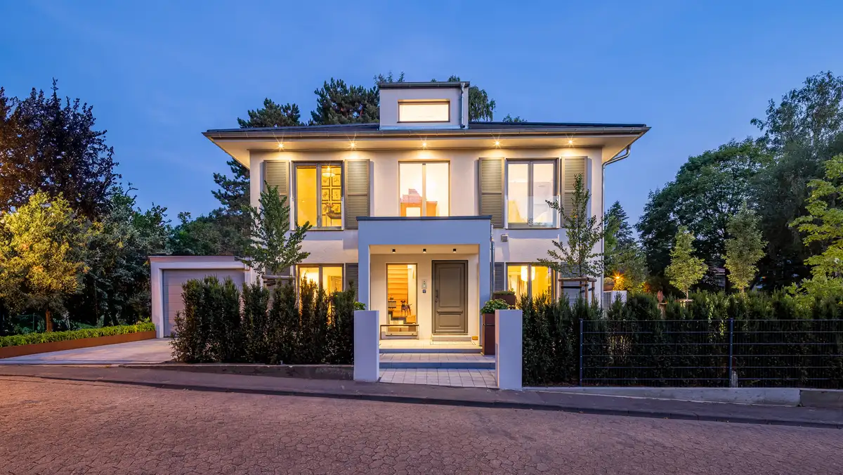 Außenaufahme bei Dämmerung von einer eleganten Stadtvilla mit Walmdach, grüne Fensterläden und Eingangsüberdachung