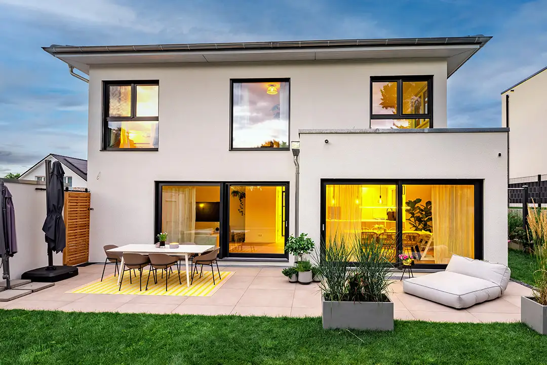 Walmdachhaus mit weißer Fassade, kleinem Flachdachanbau mit Dachterrasse und großen Fensterflächen